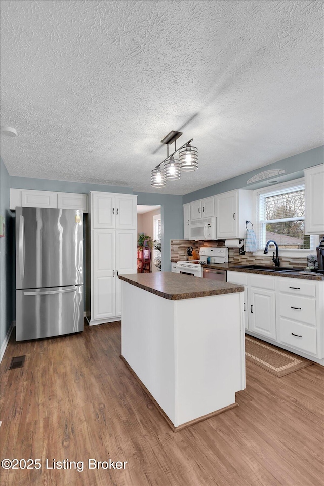 kitchen featuring dark countertops, white cabinets, white appliances, and wood finished floors