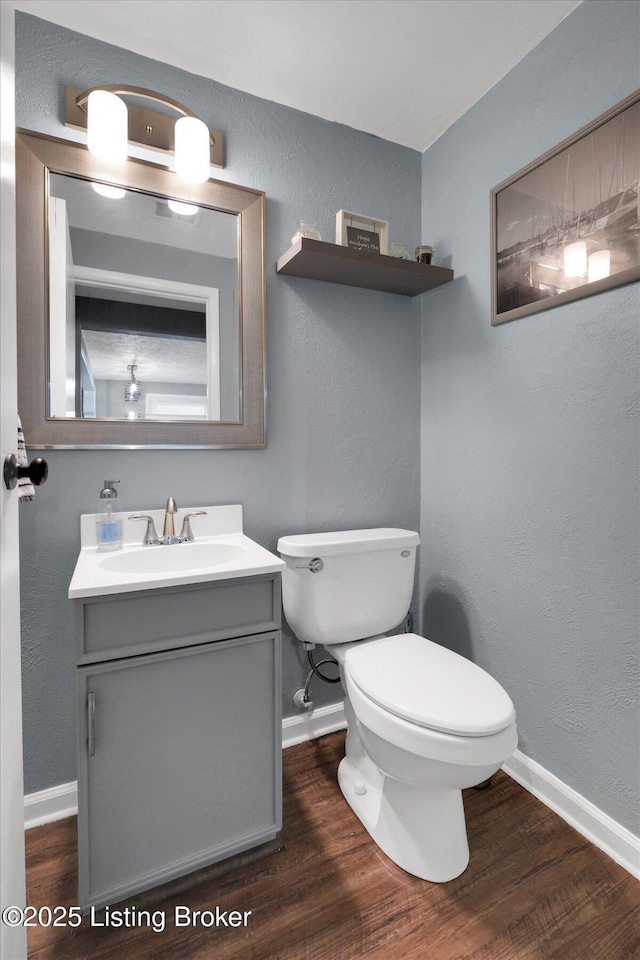 half bath with toilet, vanity, baseboards, and wood finished floors