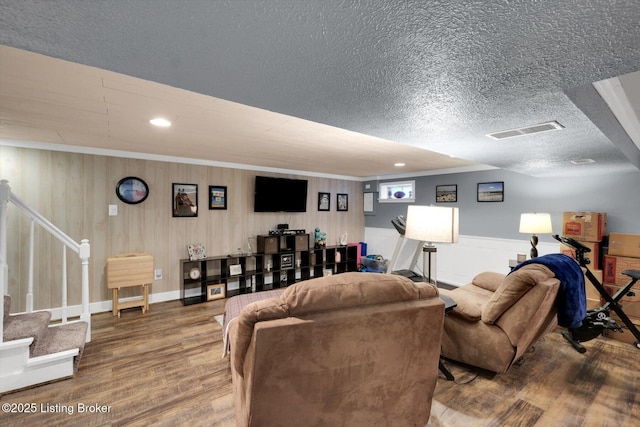 living area with a textured ceiling, stairway, wood finished floors, visible vents, and wainscoting