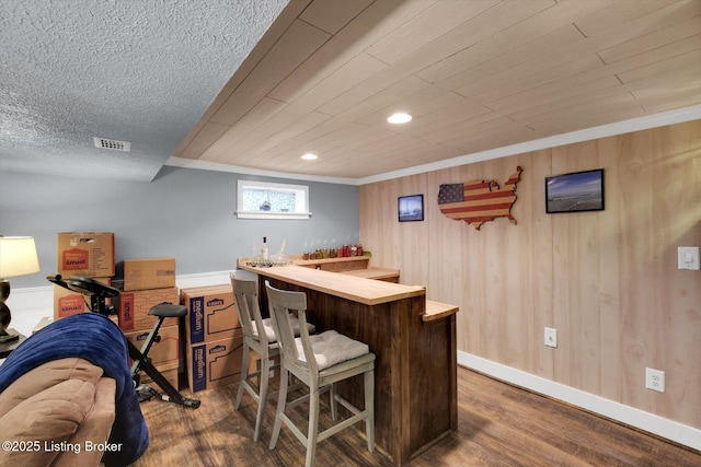 bar with wooden walls, visible vents, dark wood-type flooring, baseboards, and a dry bar