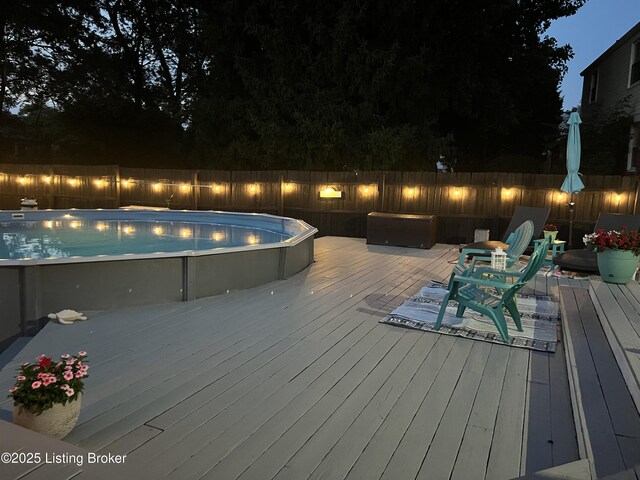 deck at twilight with a fenced backyard and a fenced in pool