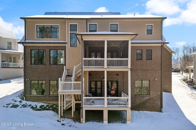 snow covered rear of property with brick siding, stairway, and a sunroom