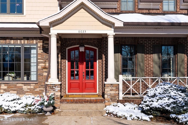 snow covered property entrance with a porch and brick siding