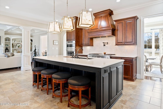 kitchen with light countertops, custom range hood, appliances with stainless steel finishes, a sink, and ornate columns