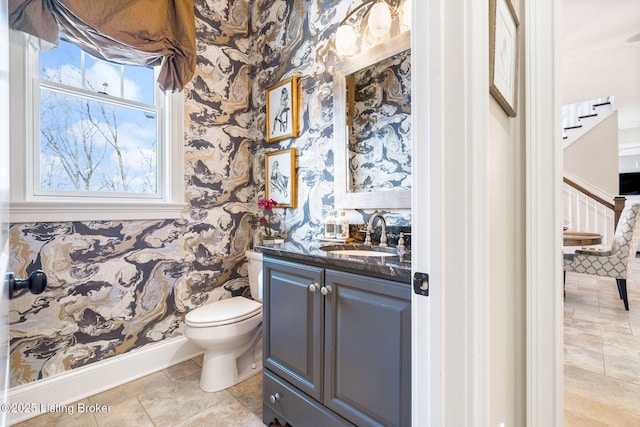 bathroom with toilet, baseboards, vanity, and wallpapered walls