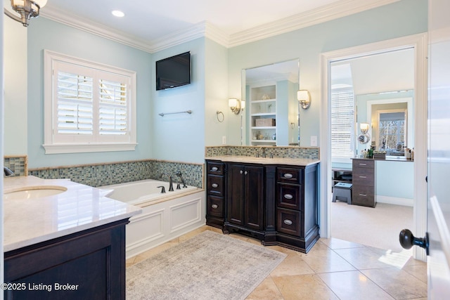 full bath featuring ornamental molding, two vanities, a sink, and a garden tub