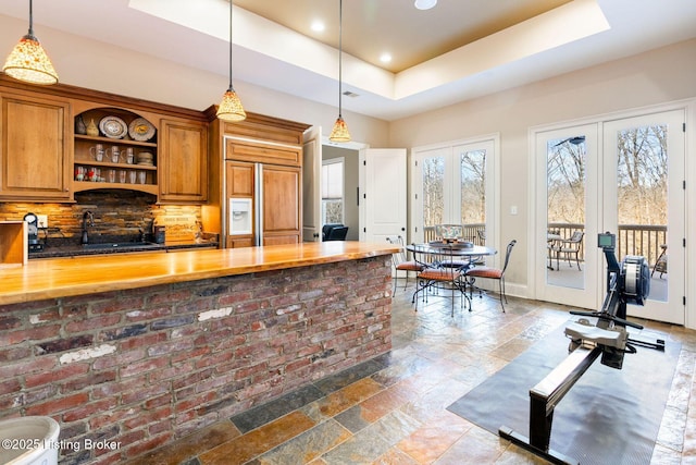 kitchen with stone tile floors, paneled fridge, a tray ceiling, and wooden counters