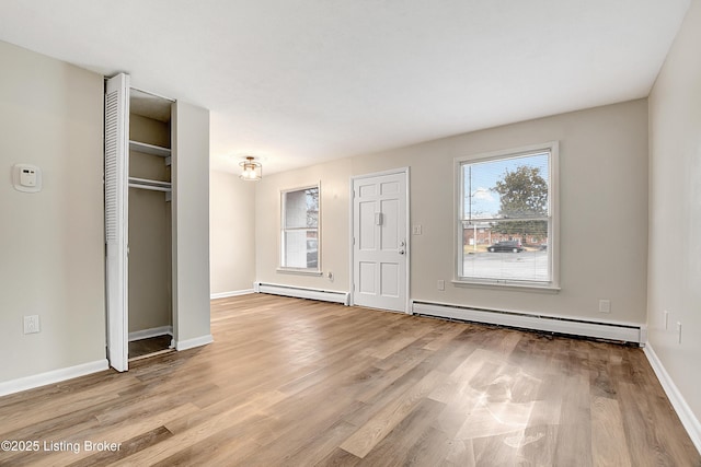 unfurnished bedroom with a baseboard heating unit, a closet, baseboards, and light wood-style floors