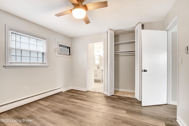 unfurnished bedroom featuring a wall unit AC, a closet, a baseboard heating unit, wood finished floors, and baseboards