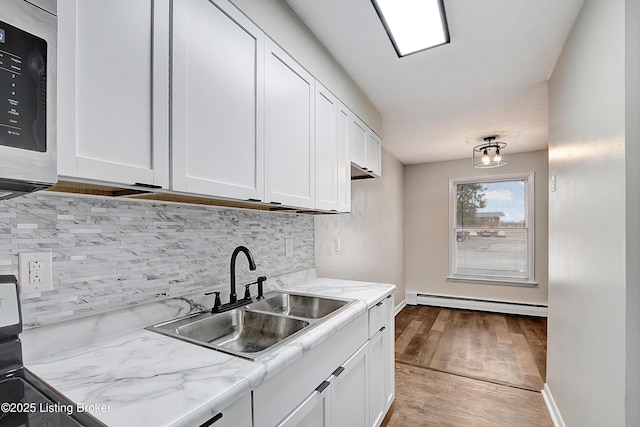 kitchen with white cabinetry, stainless steel microwave, baseboard heating, and a sink