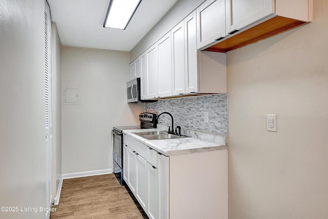 kitchen with tasteful backsplash, light countertops, appliances with stainless steel finishes, white cabinetry, and a sink