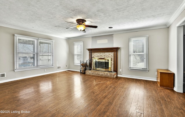 unfurnished living room featuring a ceiling fan, visible vents, wood-type flooring, crown molding, and a brick fireplace