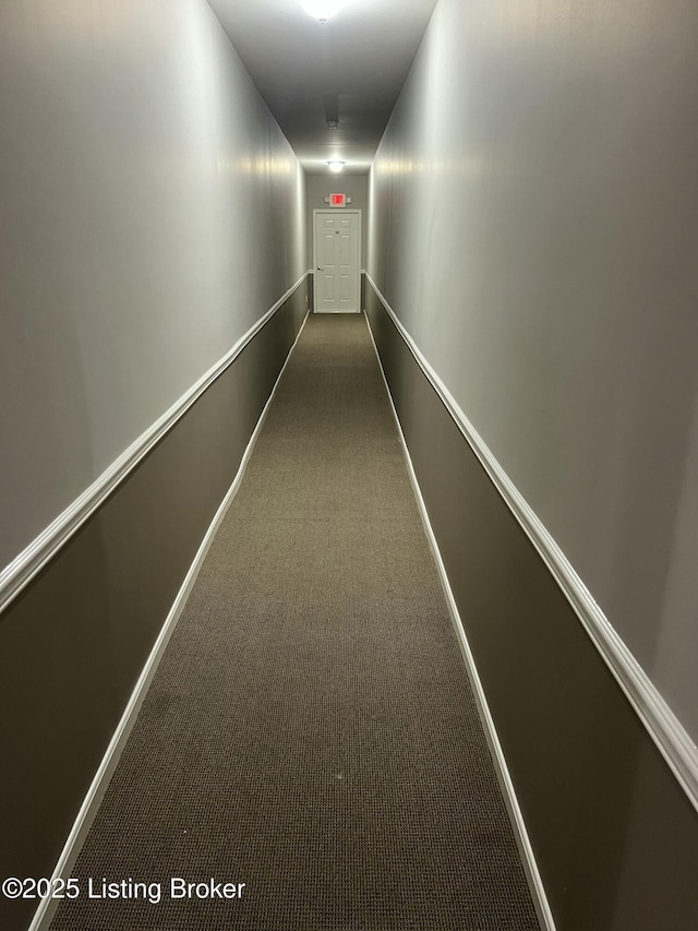 corridor featuring baseboards and dark carpet