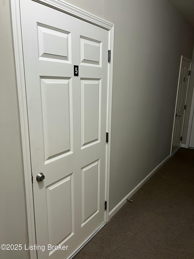 hallway with baseboards and dark colored carpet