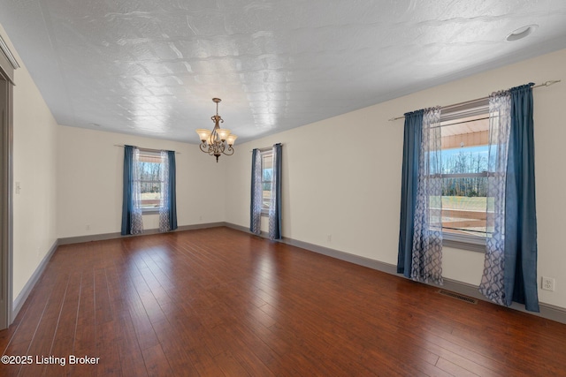 empty room featuring baseboards, wood-type flooring, visible vents, and a notable chandelier