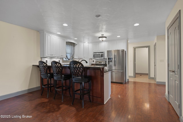 kitchen with decorative backsplash, appliances with stainless steel finishes, white cabinetry, a peninsula, and a kitchen bar