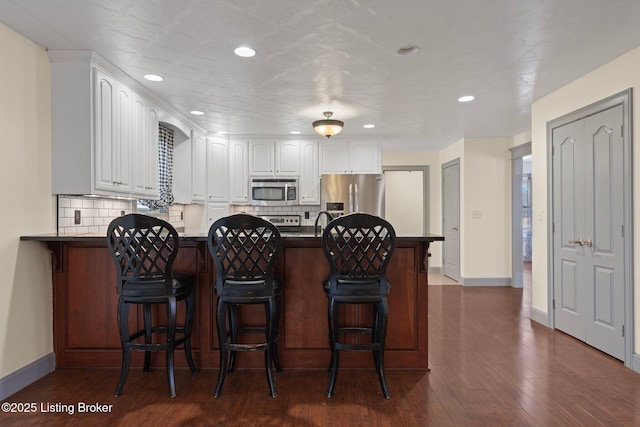 kitchen featuring a peninsula, dark wood-style flooring, white cabinetry, appliances with stainless steel finishes, and tasteful backsplash