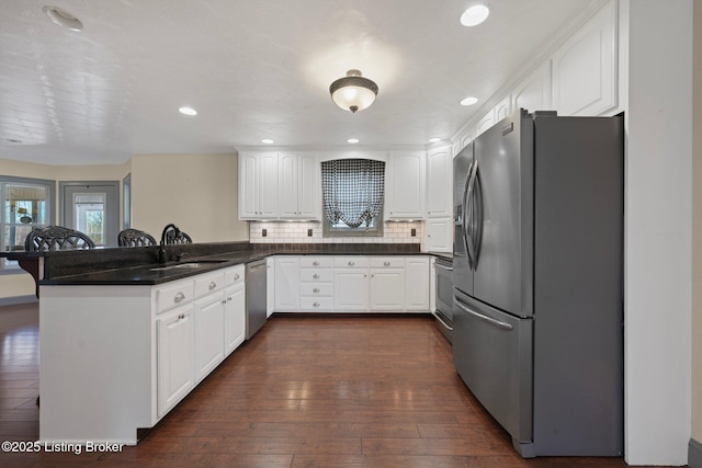 kitchen with stainless steel appliances, decorative backsplash, dark wood-type flooring, a sink, and a peninsula