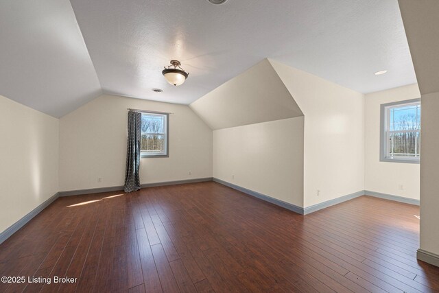 additional living space featuring lofted ceiling, hardwood / wood-style floors, a textured ceiling, and baseboards