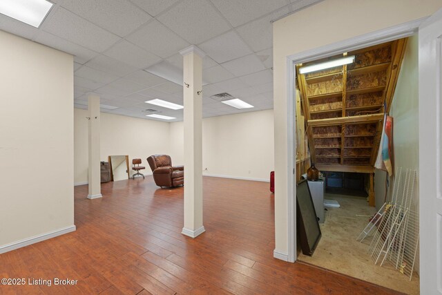 finished basement with a paneled ceiling, wood-type flooring, visible vents, and baseboards