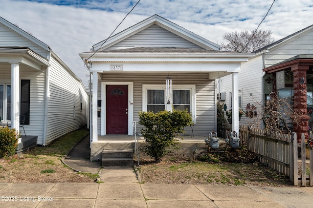 shotgun-style home featuring covered porch and fence