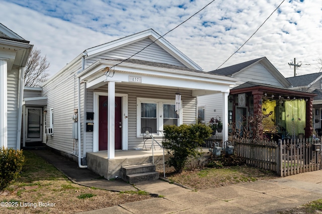 shotgun-style home featuring covered porch and fence