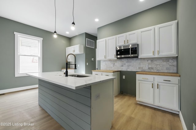 kitchen featuring stainless steel microwave, visible vents, backsplash, white cabinets, and a sink