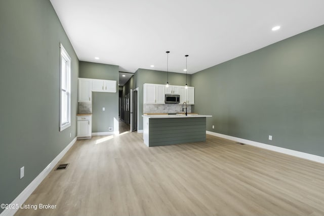 kitchen featuring visible vents, baseboards, white cabinetry, backsplash, and stainless steel microwave