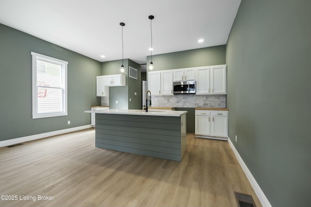 kitchen with a sink, visible vents, white cabinetry, decorative backsplash, and stainless steel microwave