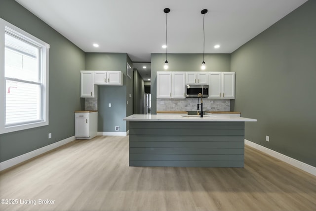 kitchen with light wood-style flooring, a sink, white cabinets, backsplash, and stainless steel microwave