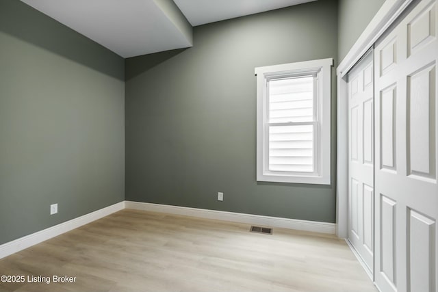 unfurnished bedroom featuring light wood-style flooring, a closet, visible vents, and baseboards