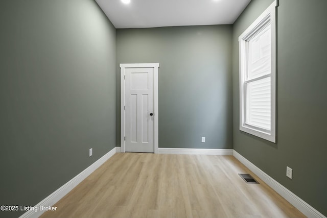 spare room featuring light wood finished floors, visible vents, and baseboards