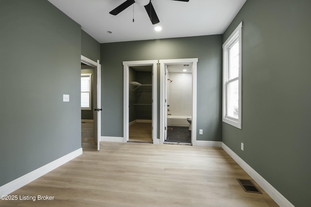 unfurnished bedroom featuring light wood-style flooring, a spacious closet, visible vents, and baseboards