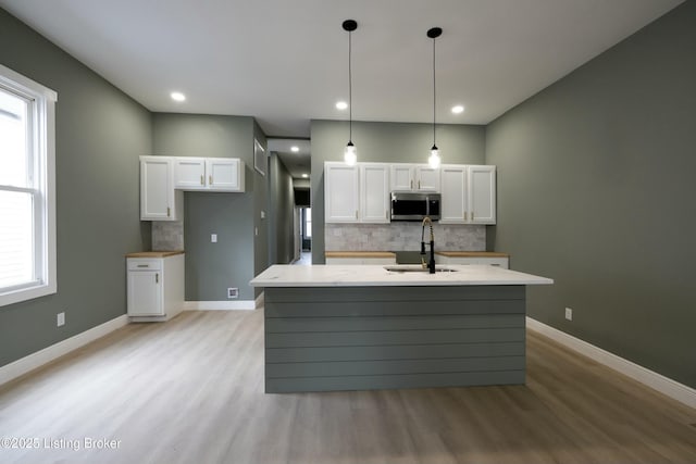 kitchen with white cabinets, stainless steel microwave, a sink, and backsplash