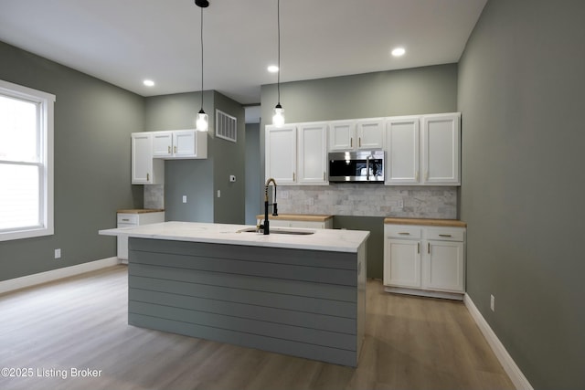 kitchen with a sink, visible vents, white cabinetry, tasteful backsplash, and stainless steel microwave