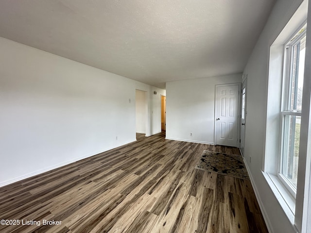 unfurnished room with dark wood finished floors, a textured ceiling, and baseboards