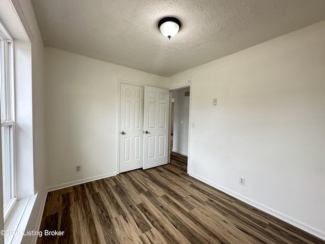 unfurnished bedroom with a closet, a textured ceiling, baseboards, and dark wood-style flooring