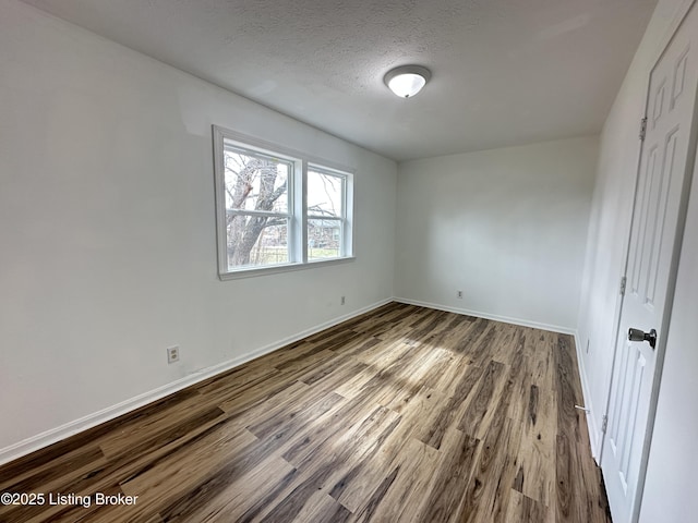 unfurnished bedroom featuring a textured ceiling, baseboards, and wood finished floors