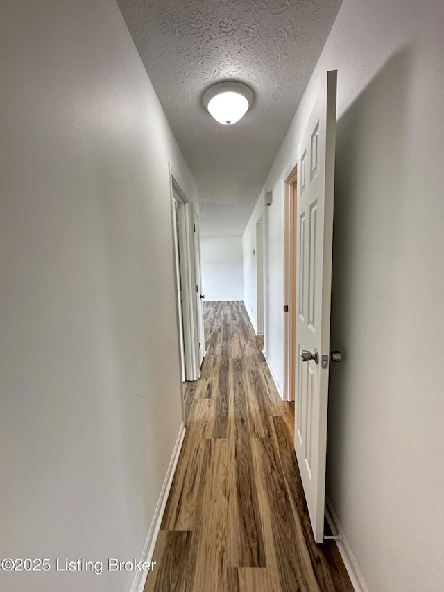 hall featuring a textured ceiling, baseboards, and wood finished floors