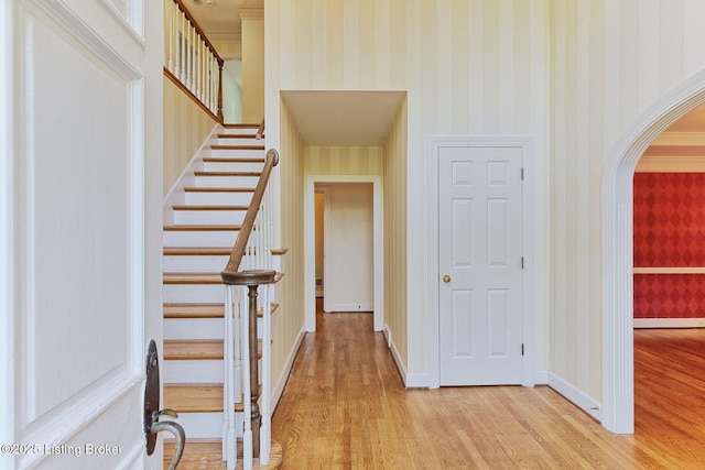 hallway featuring arched walkways, stairway, light wood-style floors, baseboards, and wallpapered walls