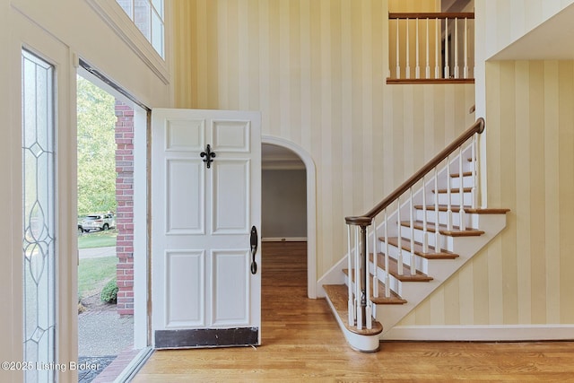 entrance foyer with wallpapered walls, light wood finished floors, baseboards, arched walkways, and stairs