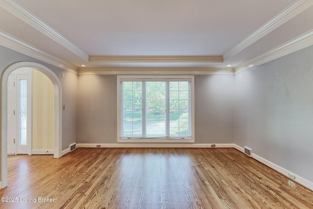 spare room featuring arched walkways, a tray ceiling, and wood finished floors