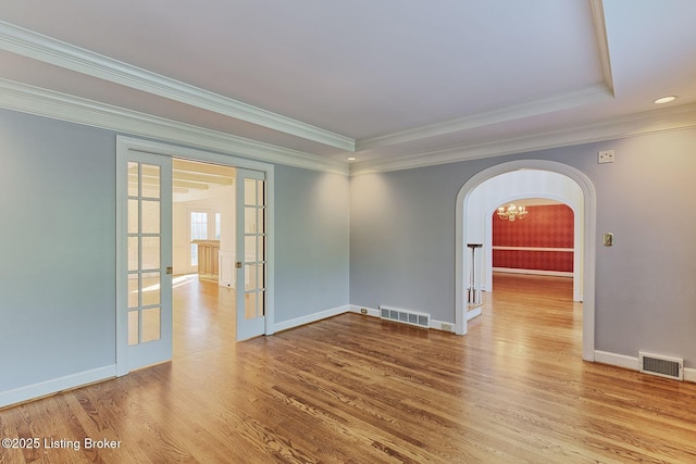 unfurnished room with arched walkways, french doors, visible vents, and wood finished floors