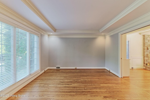 unfurnished room featuring light wood finished floors, baseboards, visible vents, ornamental molding, and a tray ceiling