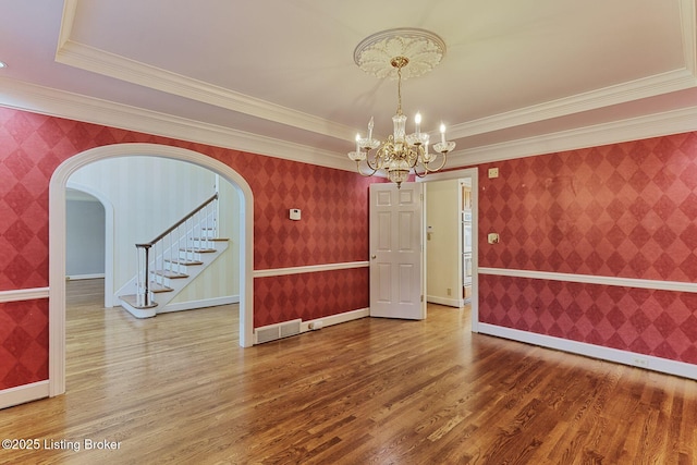 unfurnished dining area featuring wallpapered walls, baseboards, arched walkways, stairway, and wood finished floors