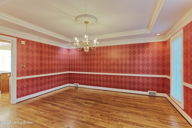 unfurnished room with wallpapered walls, visible vents, wood finished floors, an inviting chandelier, and crown molding