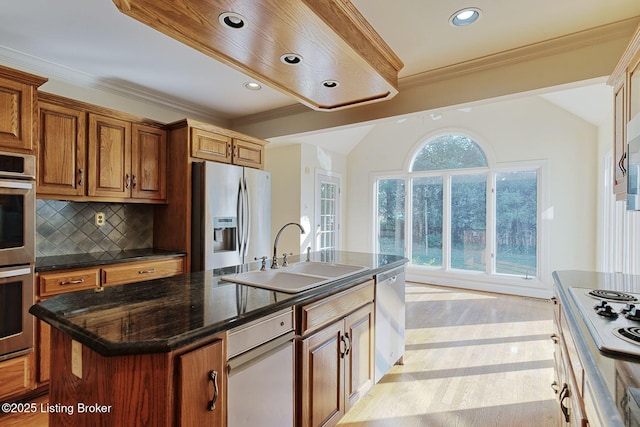 kitchen featuring stainless steel appliances, a sink, decorative backsplash, a center island with sink, and crown molding