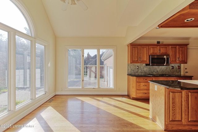 kitchen featuring dark countertops, lofted ceiling, stainless steel microwave, backsplash, and light wood-style floors