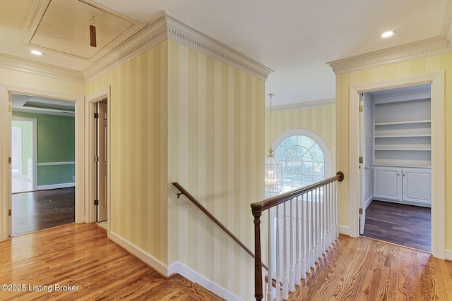 corridor featuring attic access, wood finished floors, an upstairs landing, and wallpapered walls