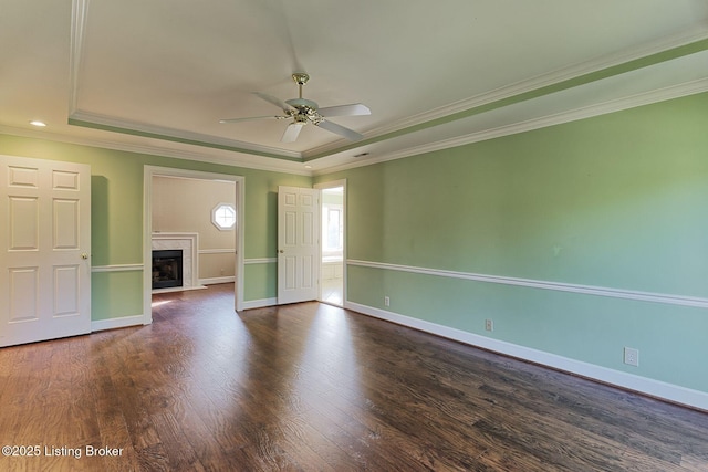 unfurnished room featuring a raised ceiling, a premium fireplace, ornamental molding, wood finished floors, and baseboards